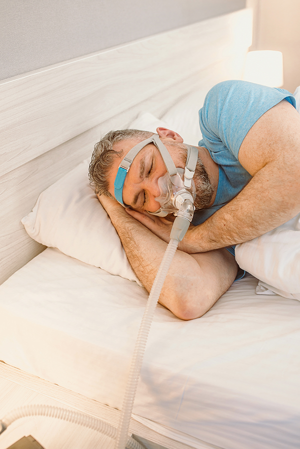 sleeping-man-with-chronic-breathing-issues-using-cpap-machine-bed